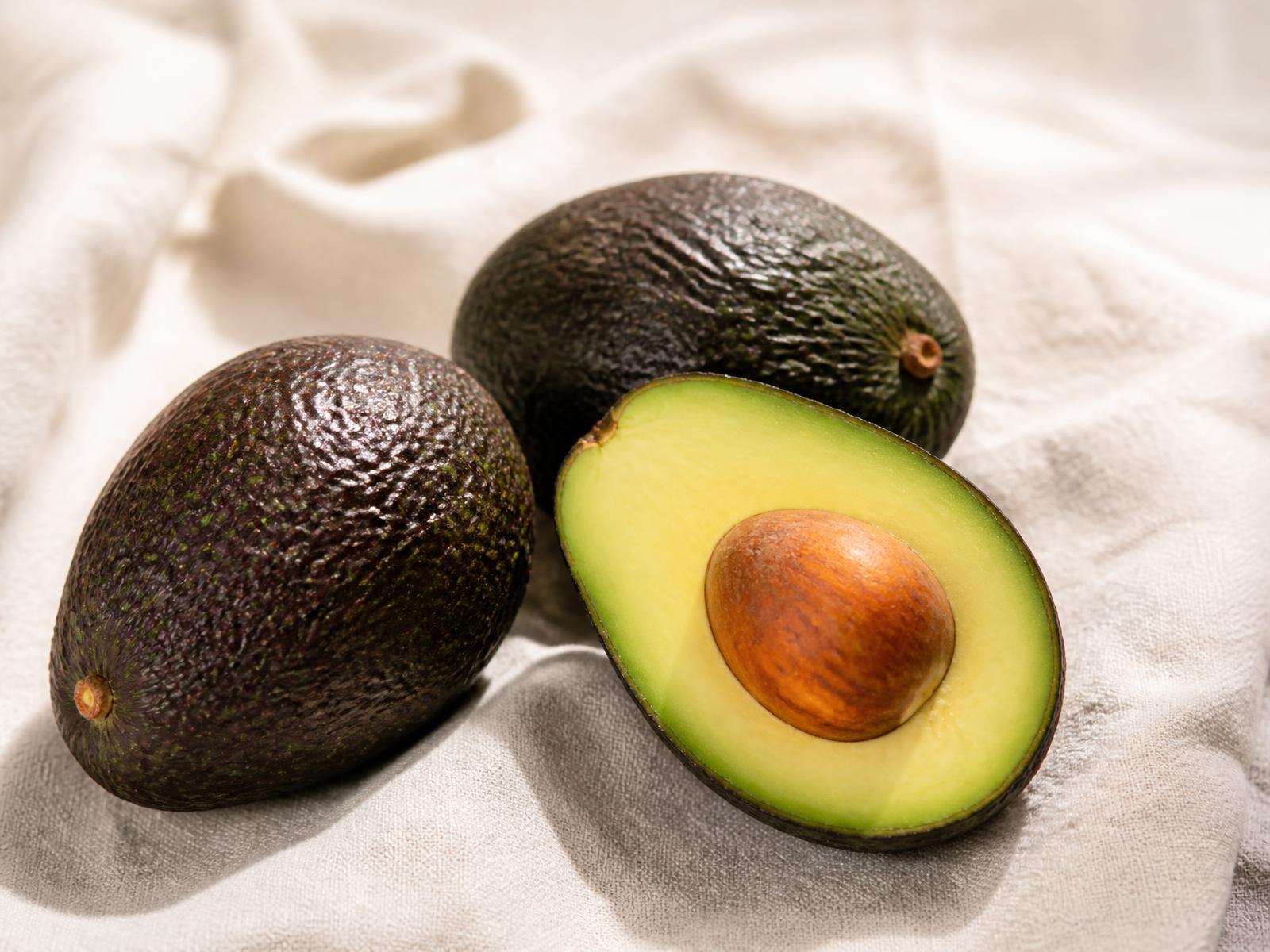 Fresh Hass avocados, one halved, on a linen surface